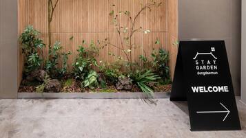 Un área de recepción con pared de paneles de madera, un cartel que dice 'STAY GARDEN dongdaemun' y un letrero de bienvenida con una flecha.