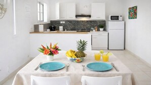 Una cocina moderna con armarios blancos, salpicadero de mármol y un comedor con mesa para dos.
