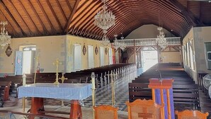 Interior de iglesia con vigas de madera, candelabro, bancales y una escalera.