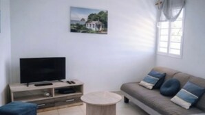 Una sala de estar con un sofá, una mesita redonda, un televisor sobre un mueble bajo y un cuadro en la pared.