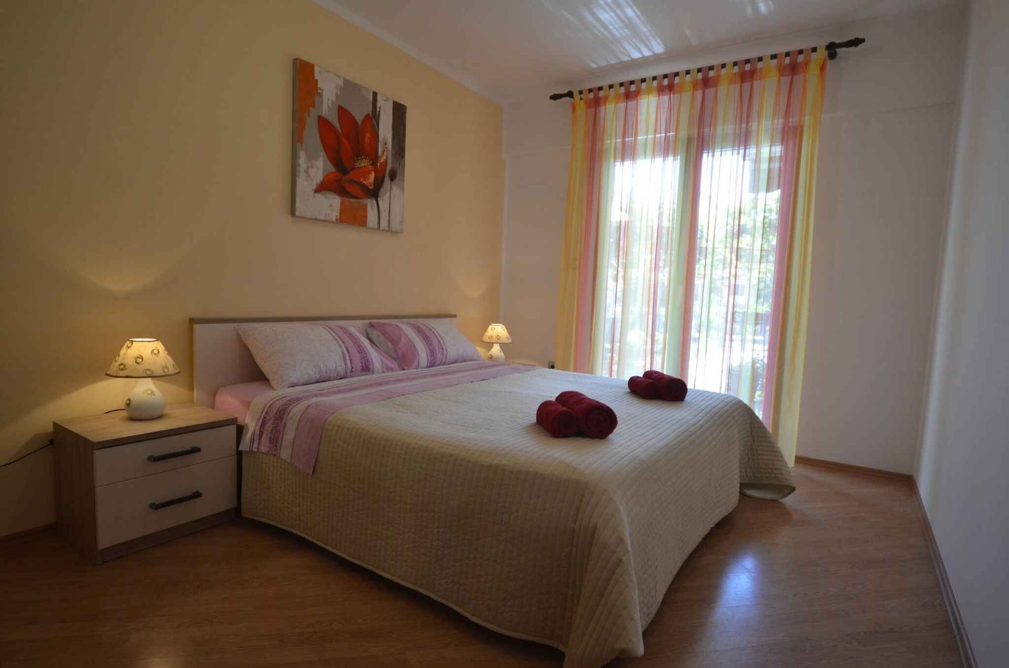 A bedroom with a bed, two bedside tables, a lamp, a painting, and a window with curtains.