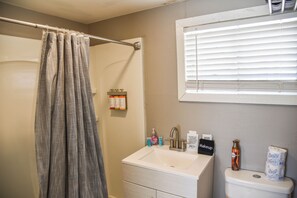Une salle de bain avec un rideau de douche, un lavabo, des toilettes et une fenêtre avec des stores.
