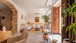 A modern living room with a sofa, coffee table, and decorative items. There is a glass door leading to an outdoor area with plants. - VILA NOVA SUITES & SPA - DOBLE SUPERIOR CON BALCÓN (Capdepera)