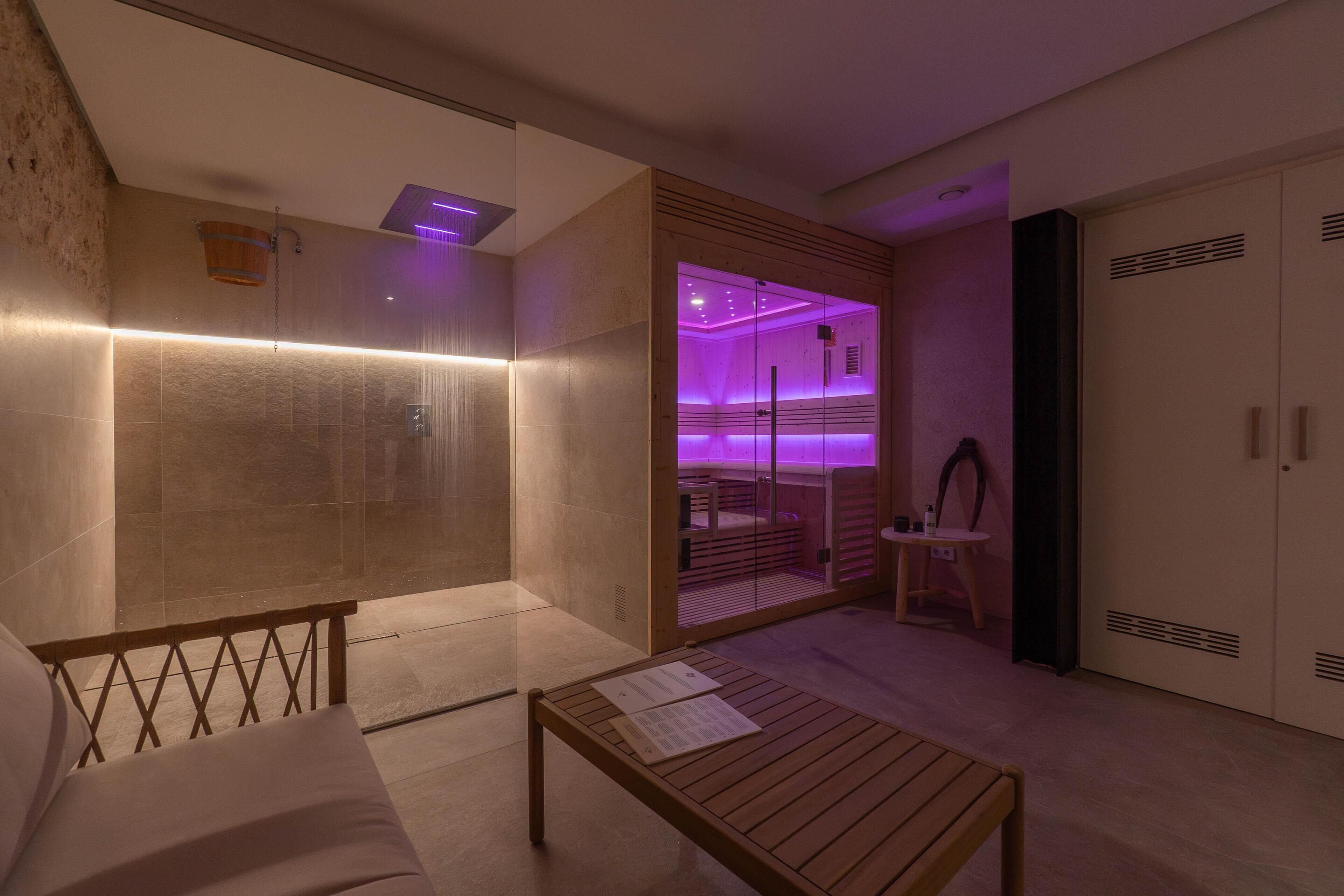 Un baño moderno con cabina de ducha de vidrio, un banco de madera y una mesita con un libro.
