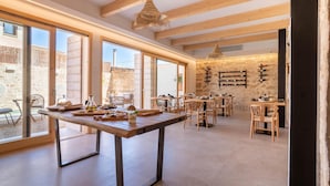 A spacious dining area with large windows, wooden beams, and a rustic stone wall. - VILA NOVA SUITES & SPA - DOBLE SUPERIOR CON BALCÓN (Capdepera)