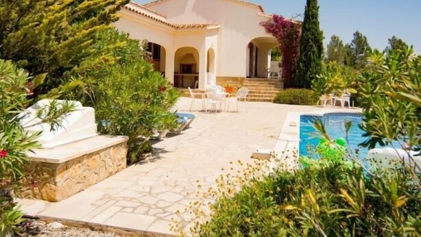 En villa med swimmingpool, udendørs møbler og have.
