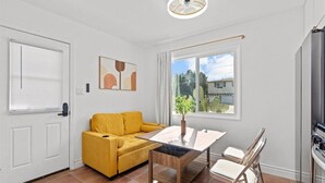 Ein modernes Wohnzimmer mit einem gelben Sofa, einem Couchtisch mit Glasplatte und einem Essbereich mit weißem Tisch und Stühlen.