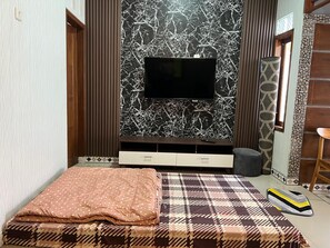 A bedroom with a bed, a television mounted on a marble wall, a small cabinet, and a patterned rug. - Tano Homestay Bromo (Ngadisari)
