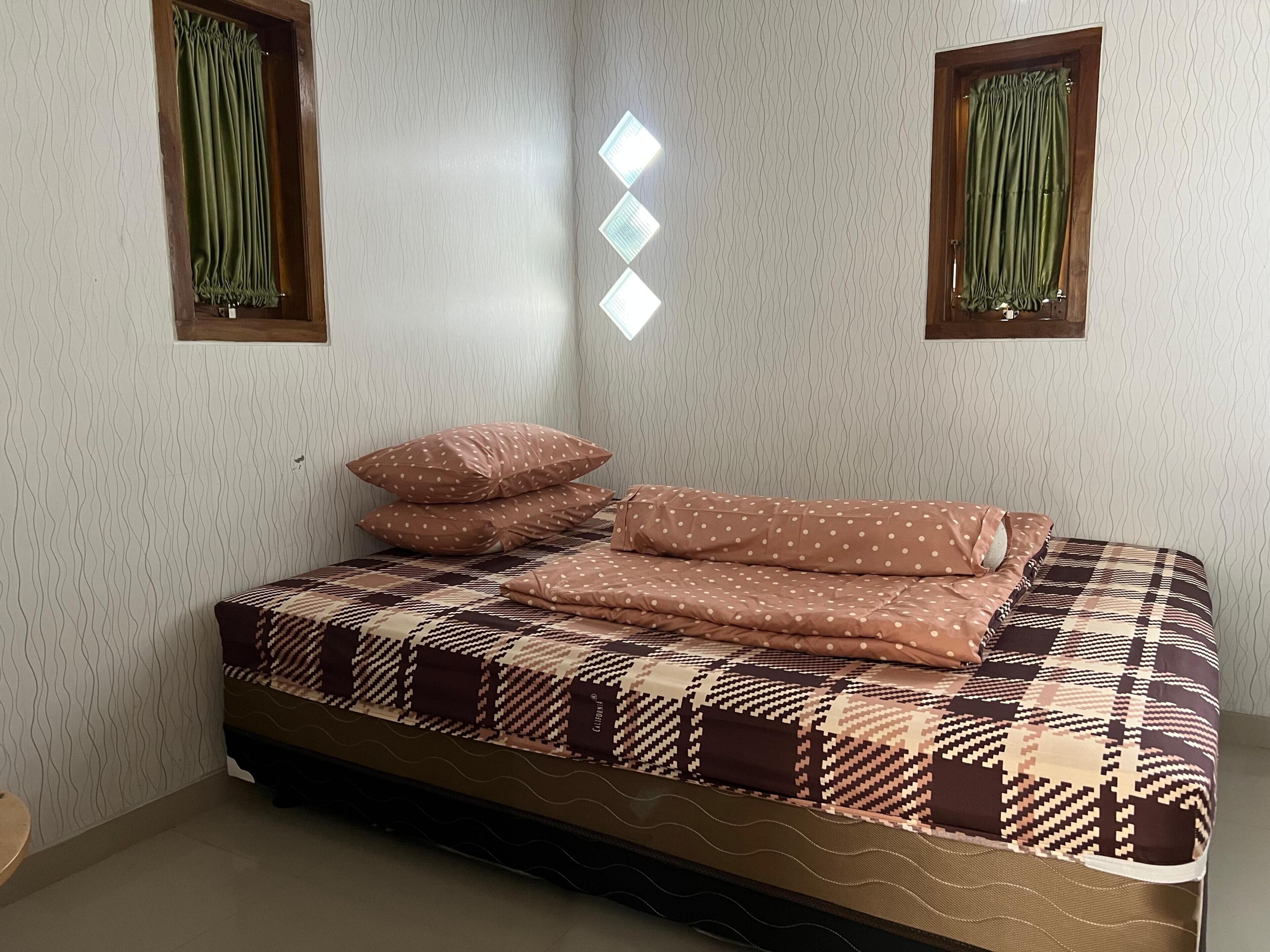 Una cama con colcha estampada, almohadas y colchón en una habitación con papel tapiz y cortinas decoradas.