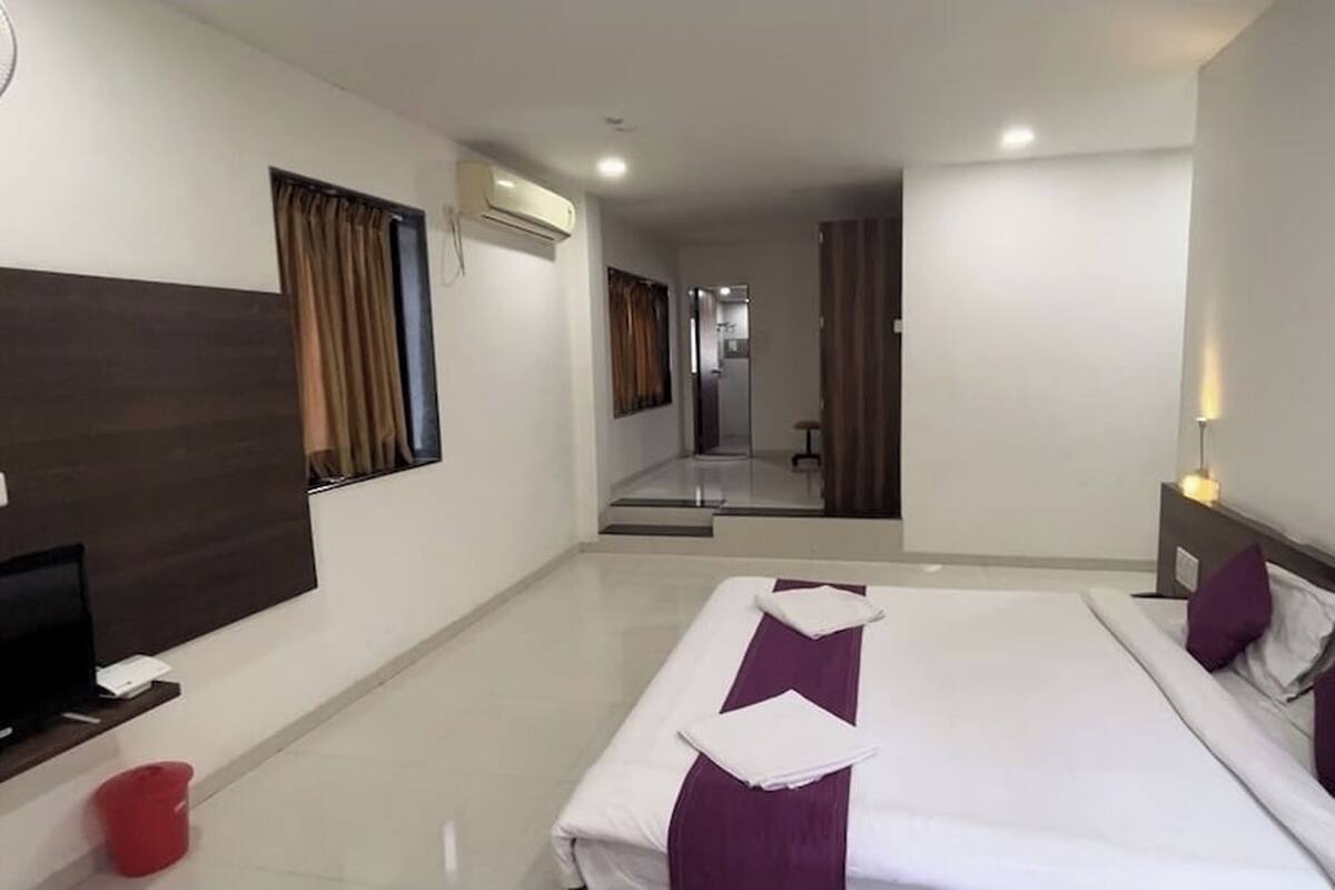 A hotel room with a large bed, a TV, a red bucket, and a mirror.
