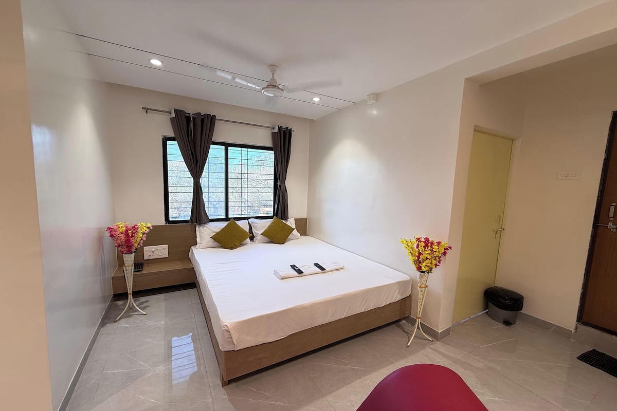 Une chambre d’hôtel moderne avec un grand lit, une table de chevet, une fenêtre avec des rideaux, une petite table ornée de fleurs et une porte.