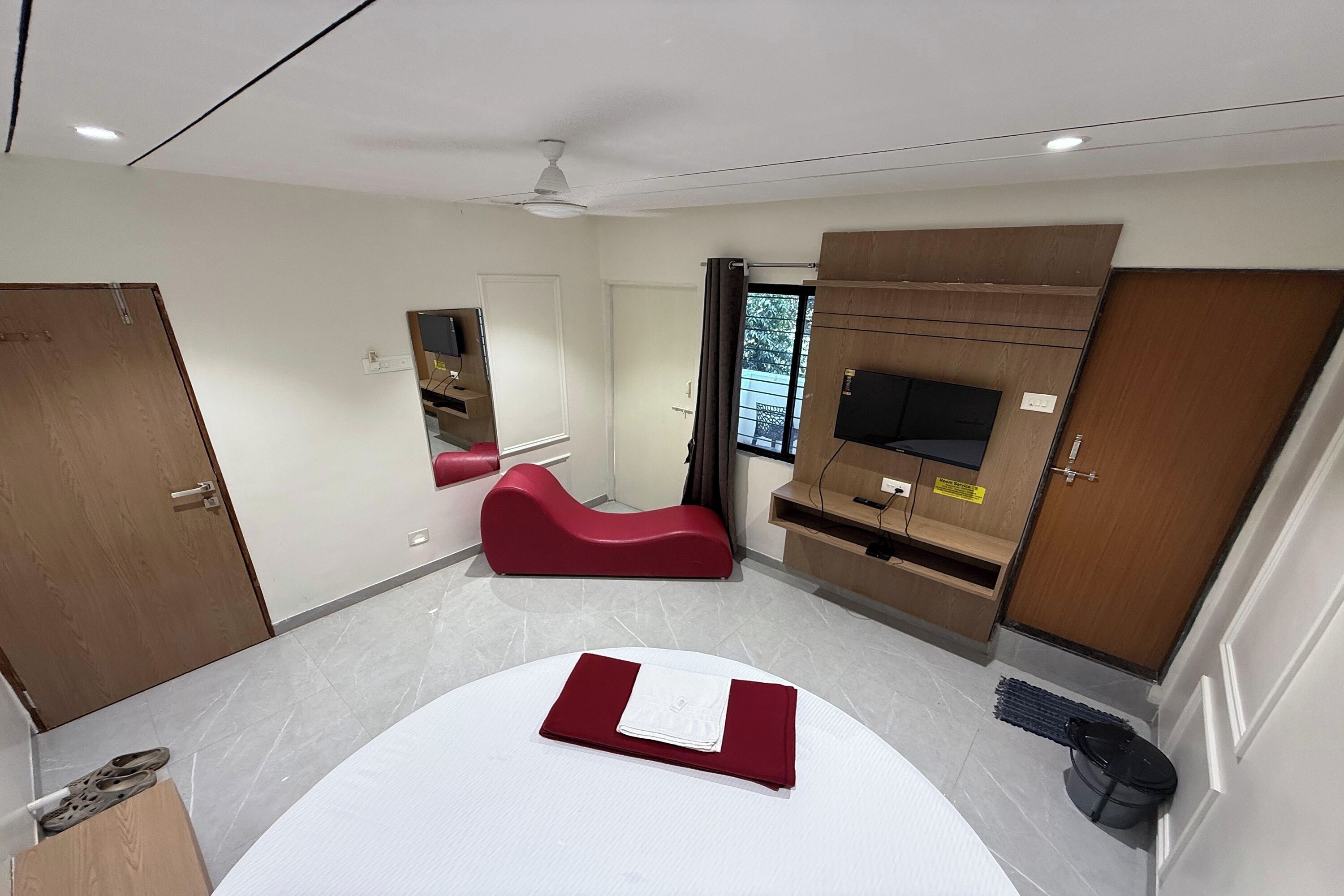 Una habitación de hotel moderna con una cama curvada, un sofá rojo, un televisor y un armario de madera.