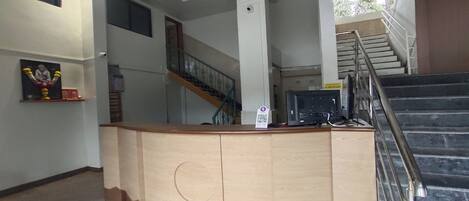 Un mostrador de recepción con detalles de madera, una escalera con barandillas metálicas y una cámara de seguridad instalada en la pared.