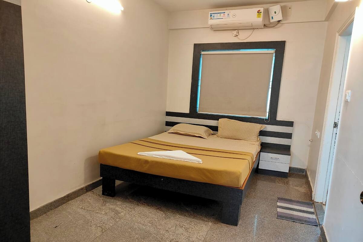 Ein kleines, ordentlich eingerichtetes Schlafzimmer mit Bett, Nachttisch und einem Fenster mit Jalousien.