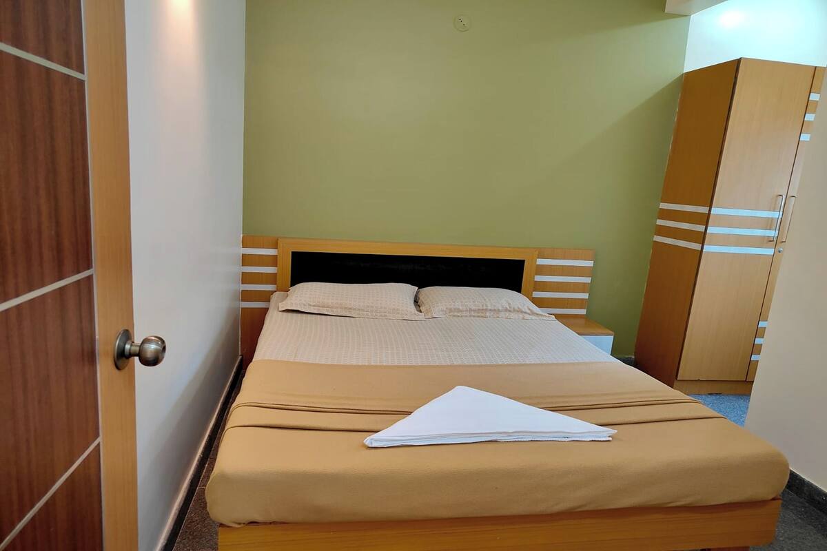 Ein ordentlich bezogenes Bett mit beiger Bettdecke und Kissen, ein Holz-Kopfteil und ein Holzschrank mit horizontalen Streifen.