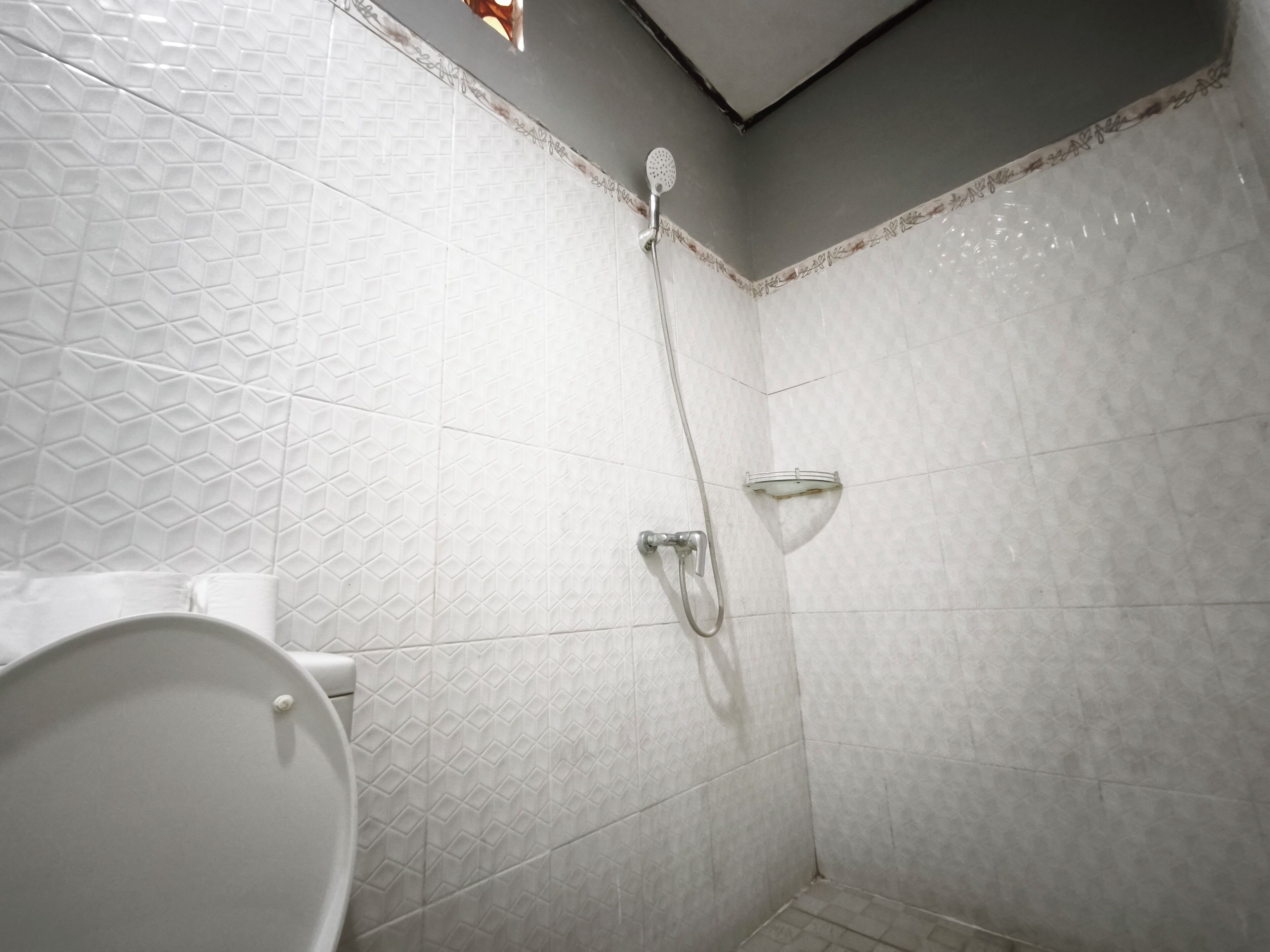 Kylpyhuone, jonka seinät on laatoitettu valkoisilla laatoilla, ja jossa on suihku sekä wc.