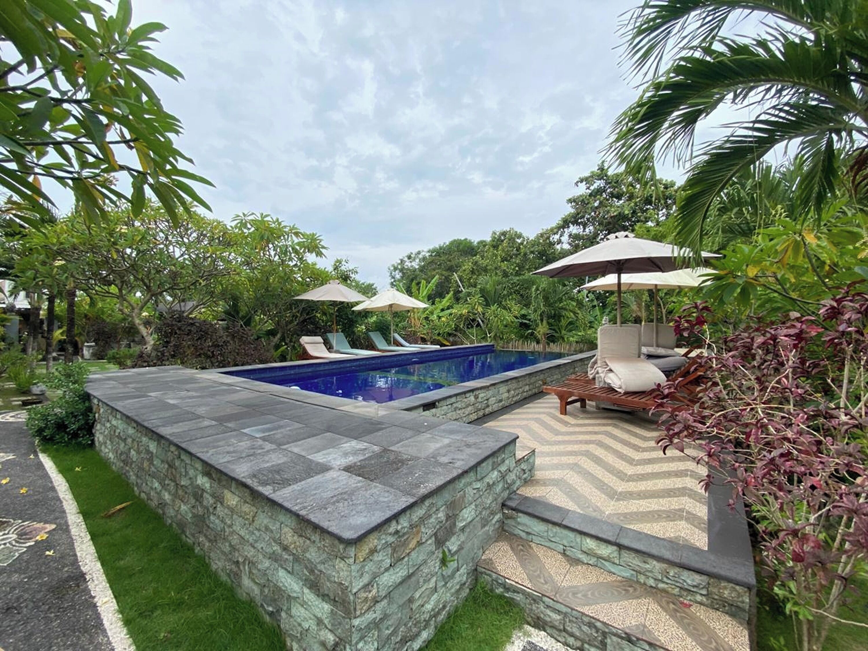 A swimming pool with lounge chairs and umbrellas, surrounded by greenery.