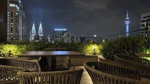 An outdoor seating area with wicker chairs and a table, overlooking a cityscape with illuminated buildings and a tower. - Majestic Residence Klcc By Luxe (Kuala Lumpur)