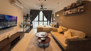 A modern living room with a sofa, coffee table, and TV. There is a ceiling fan, a bookshelf, and a window with curtains. - Majestic Residence Klcc By Luxe (Kuala Lumpur)