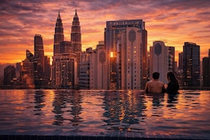 A cityscape with the Petronas Towers and a Platinum building, a couple in a pool, and a sunset. - Majestic Residence Klcc By Luxe (Kuala Lumpur)