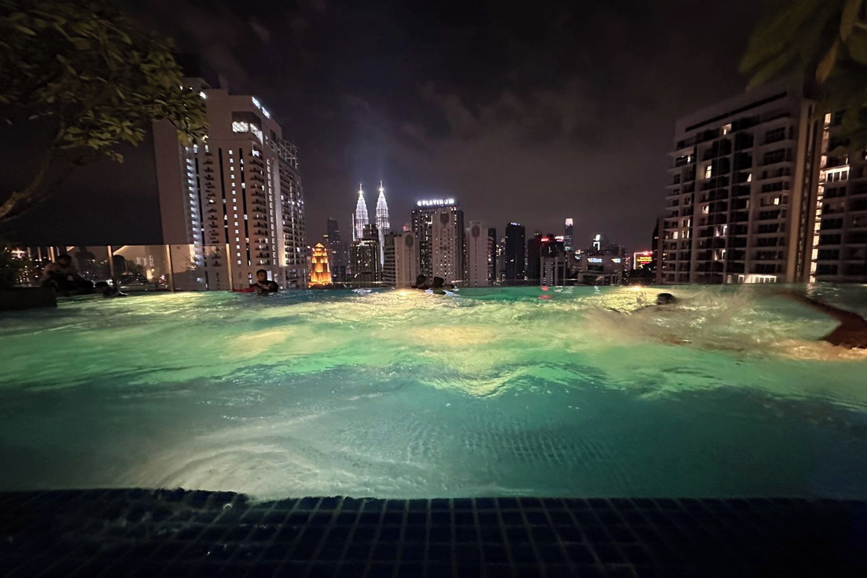 A swimming pool with a cityscape in the background, including tall buildings and a prominent tower.