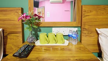 A wooden table with a vase of flowers, three green mugs, a water bottle, and a remote control.