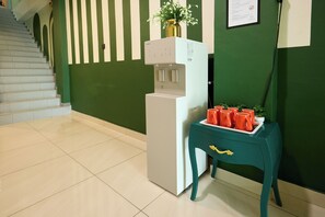 A reception area with a water dispenser, a coffee station with red mugs, and a staircase in the background.
