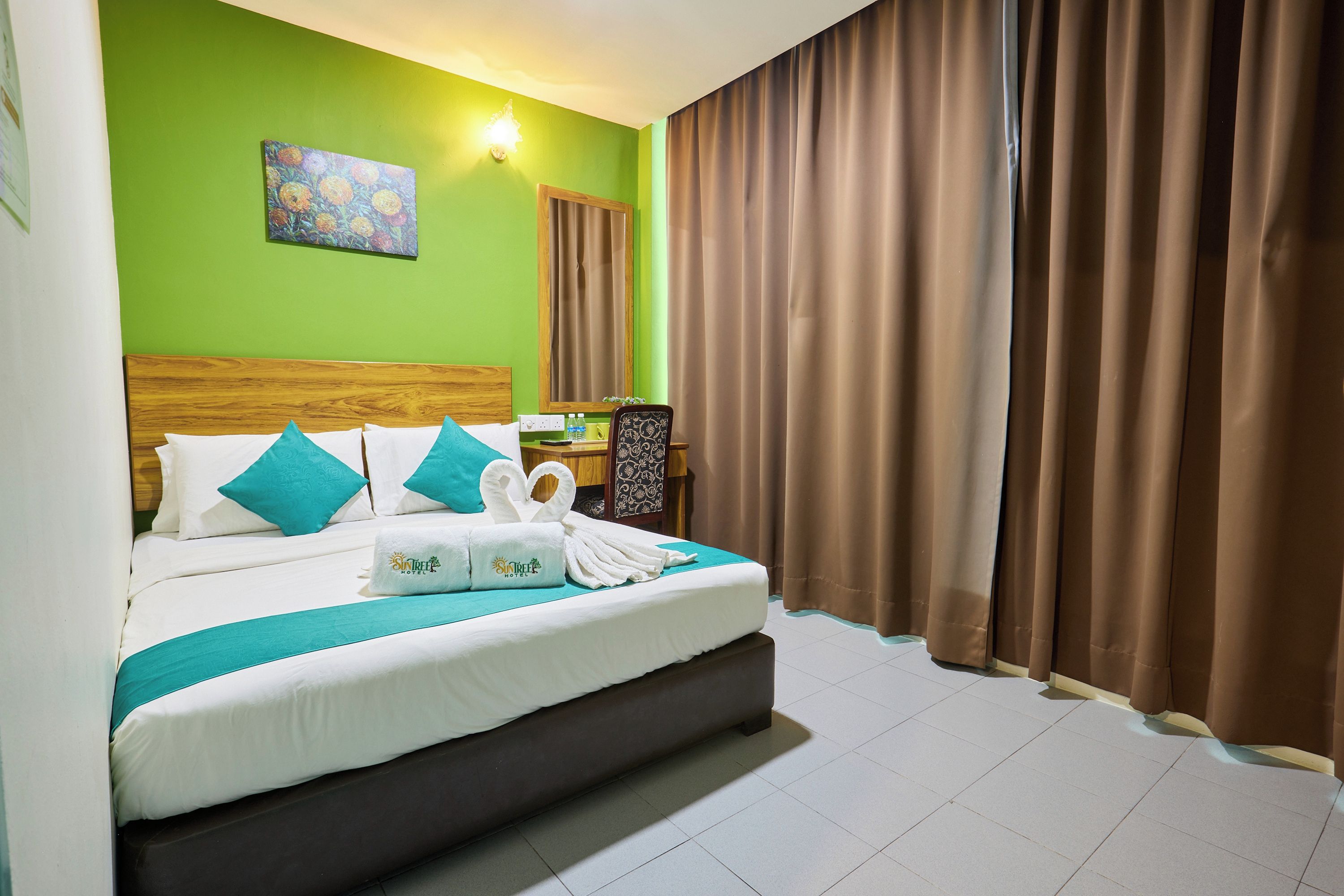A hotel room with a large bed, a headboard, a painting on the wall, and a window with curtains.