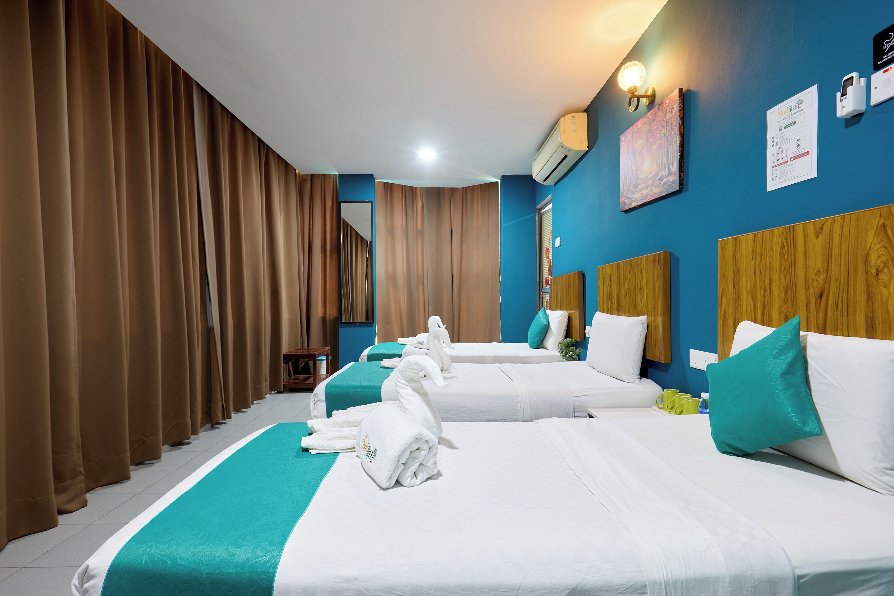 A hotel room with two beds, a blue accent wall, and a large window with curtains.
