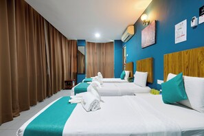 A hotel room with two beds, a blue accent wall, and a large window with curtains.