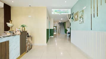 A hotel reception area with a marble counter, a reception desk, a staircase, and a wall with framed floral artwork.
