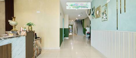 Zona de recepción de hotel con mostrador de mármol, escritorio, una escalera y una pared decorada con arreglos florales enmarcados.