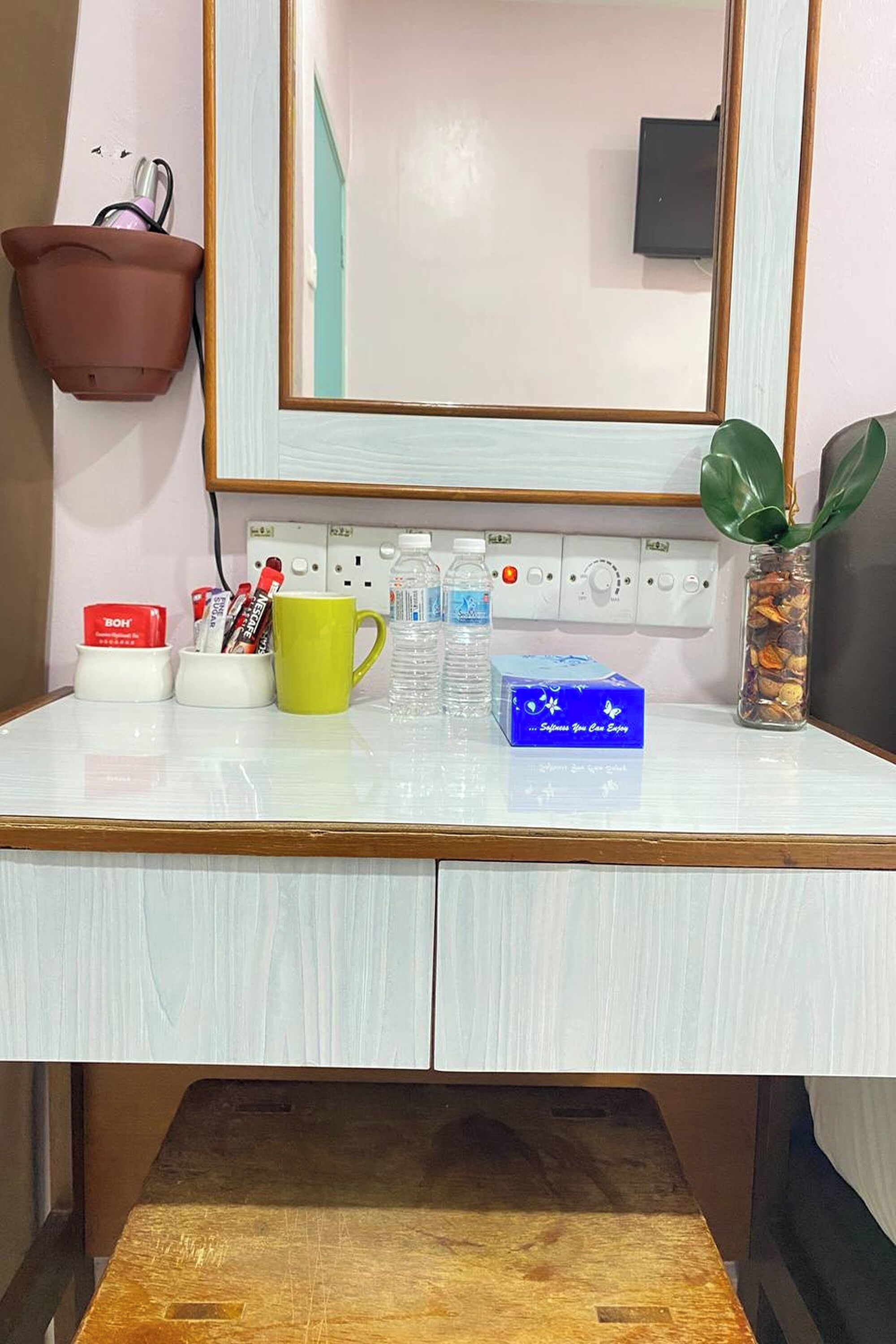 Een hotel bureau met een spiegel, een plant in pot, toiletartikelen en een waterfles.