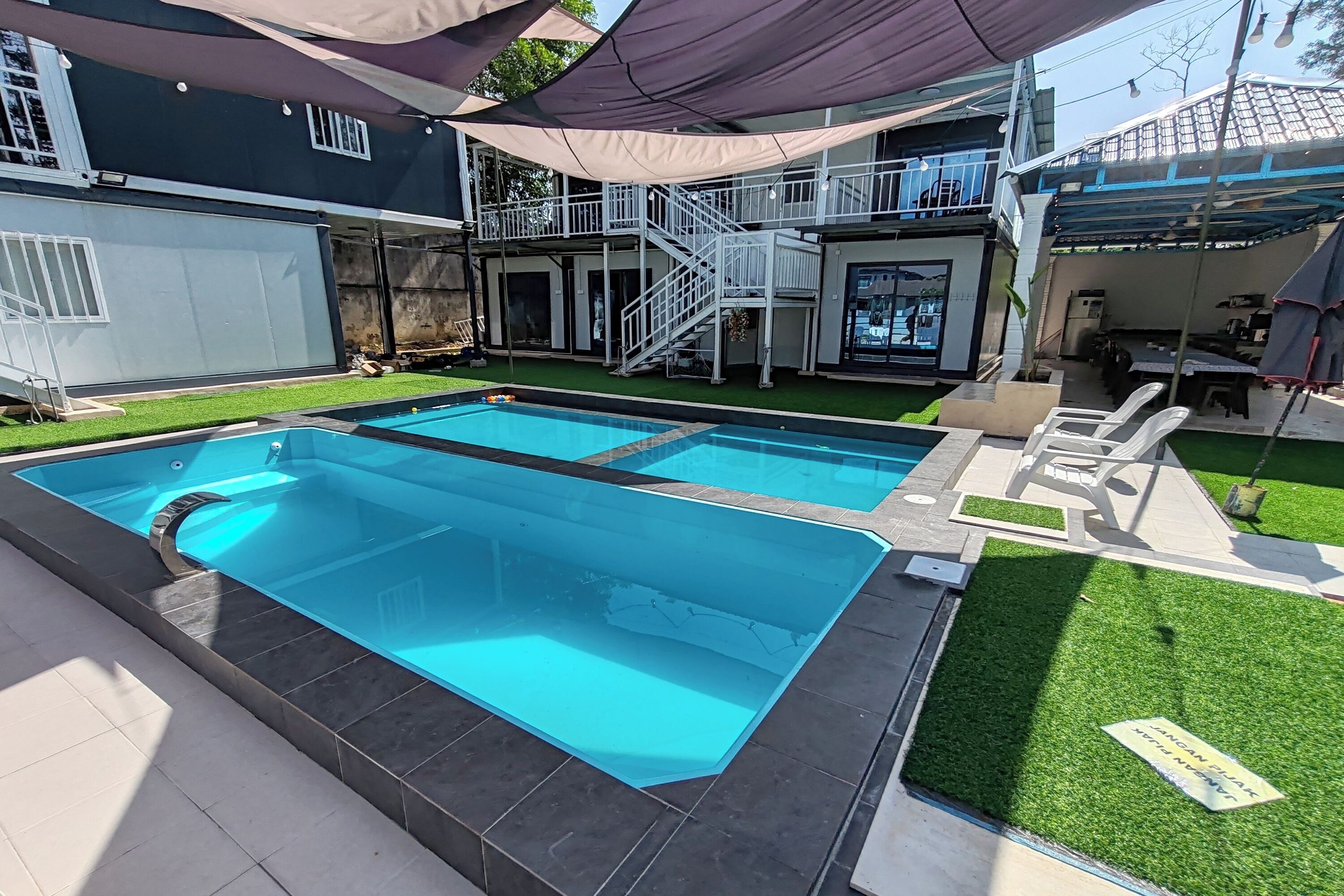 Una piscina con fondo de cristal, rodeada por un patio con sillas y una zona de estar cubierta.