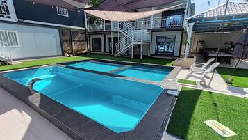 Una piscina con fondo de cristal, rodeada por un patio con sillas y una zona de estar cubierta.