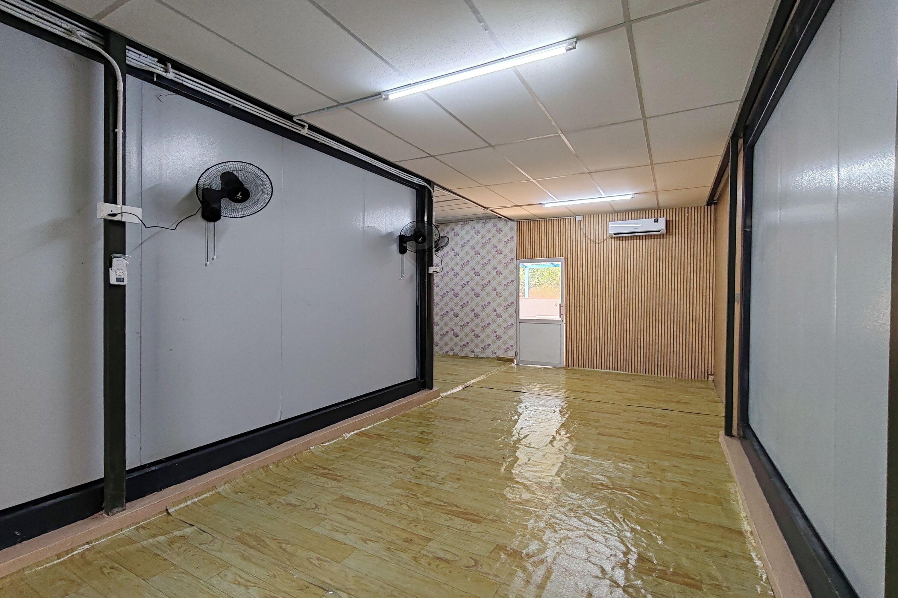 A hallway with a wooden floor, a wall-mounted fan, and an air conditioning unit.