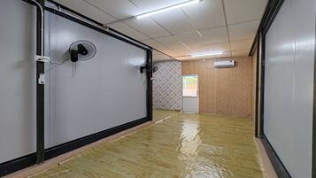 A hallway with a wooden floor, a wall-mounted fan, and an air conditioning unit.
