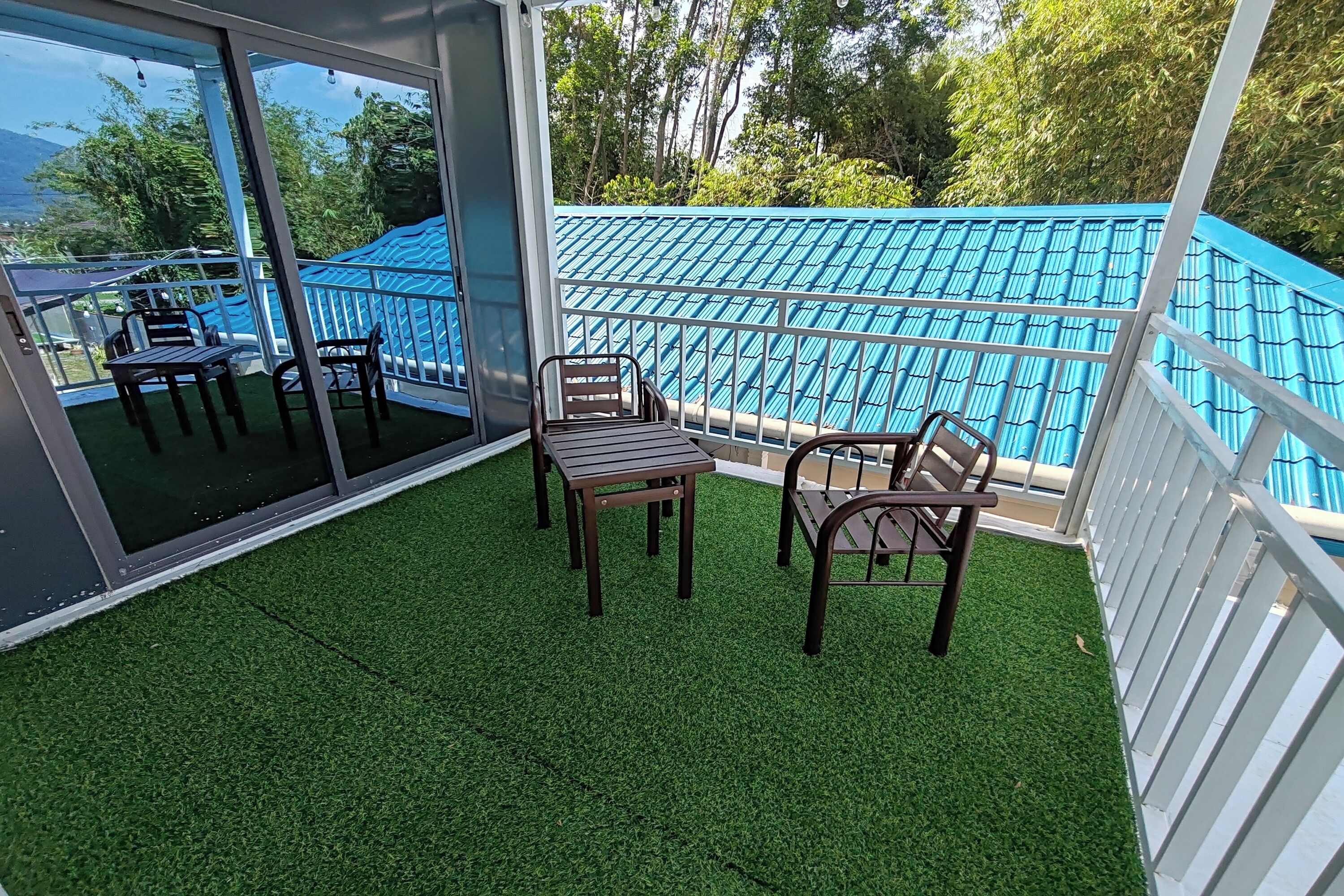 Un balcon avec un revêtement de sol en gazon synthétique, des garde-corps en métal et des chaises en bois.