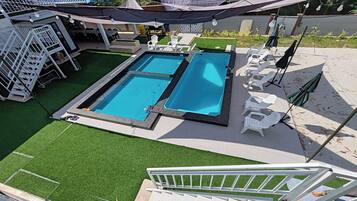A rooftop pool with two separate sections, surrounded by artificial grass, white lounge chairs, and umbrellas.