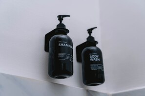 Two black bottles of shampoo and body wash on a white wall.