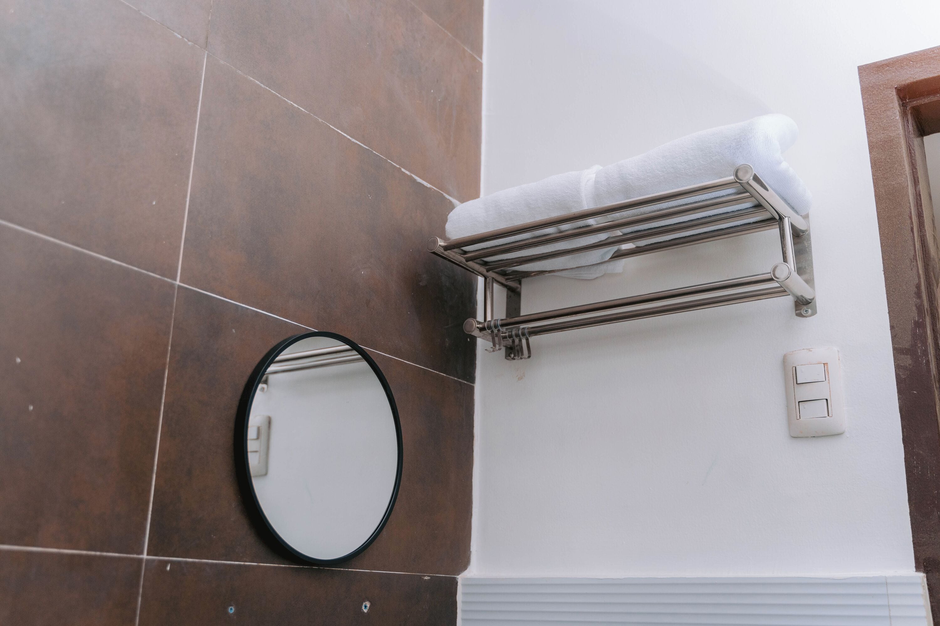 A bathroom with brown tiles, a towel rack with a white towel, a mirror, and a light switch.