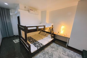 Habitación con literas, escritorio, lámpara, una alfombra pequeña y un equipo de aire acondicionado en la pared.