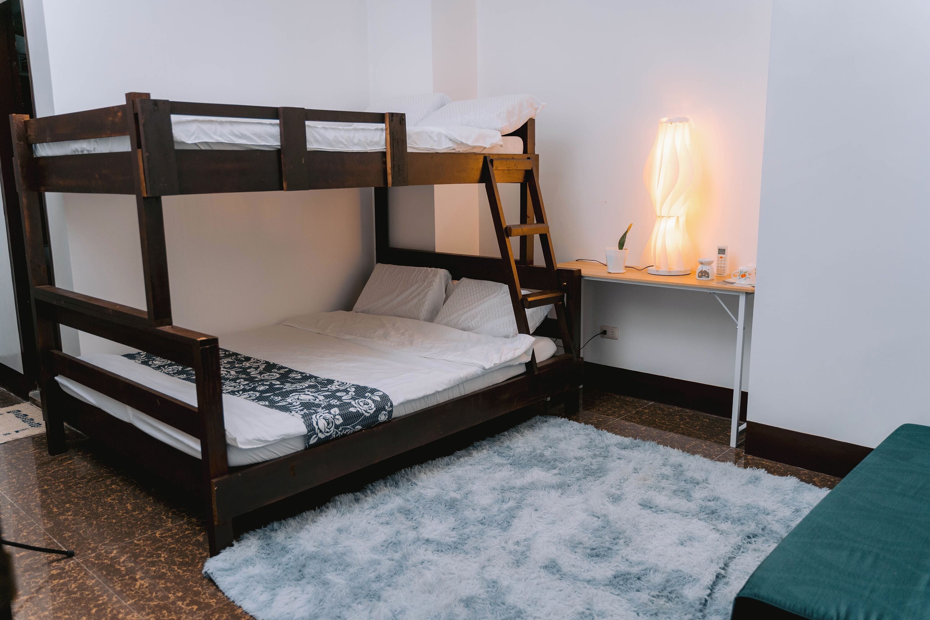 A bunk bed with a desk and lamp, a fluffy rug, and a small green bedspread.