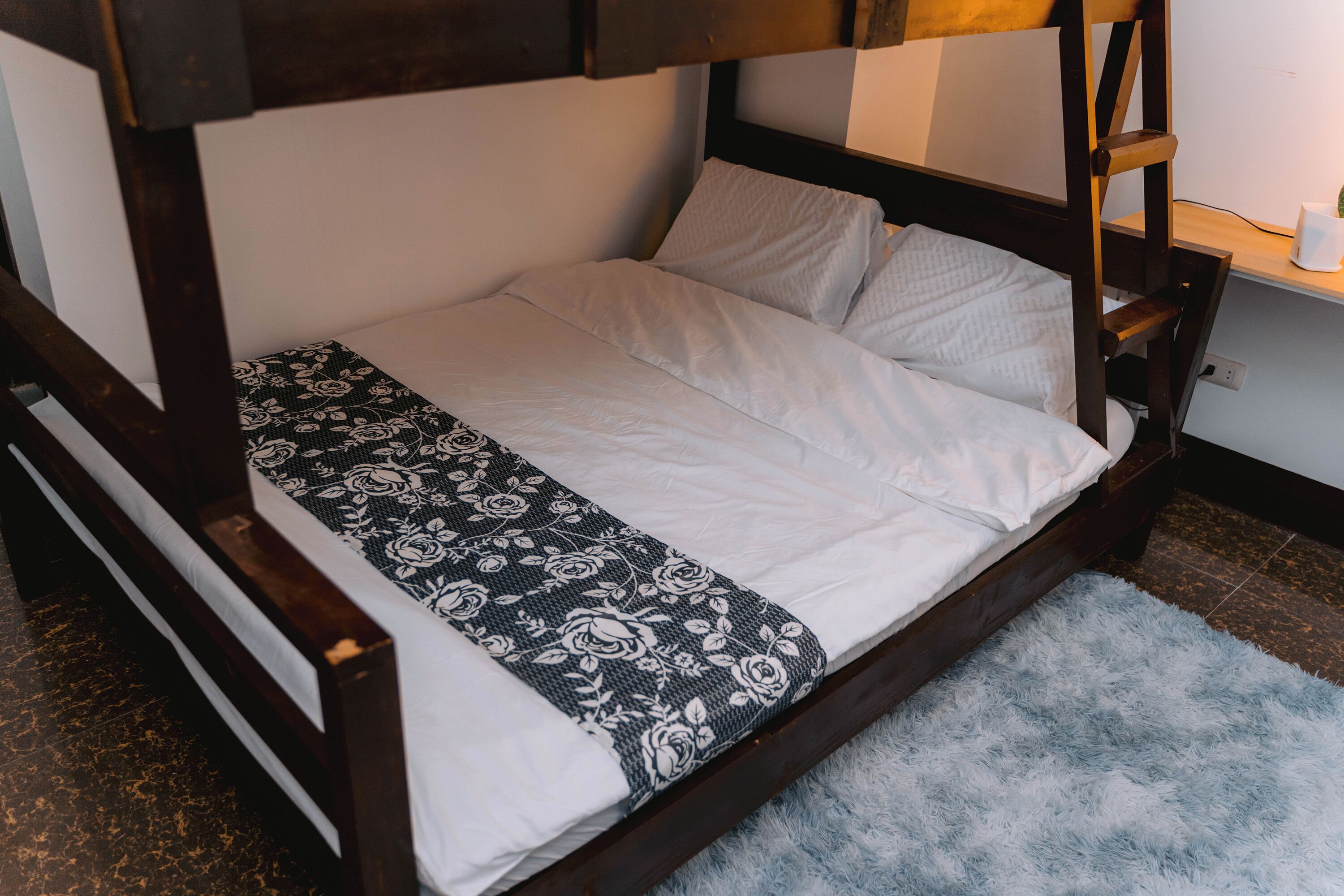 A single bed with a wooden frame, white bedding, and a patterned throw.