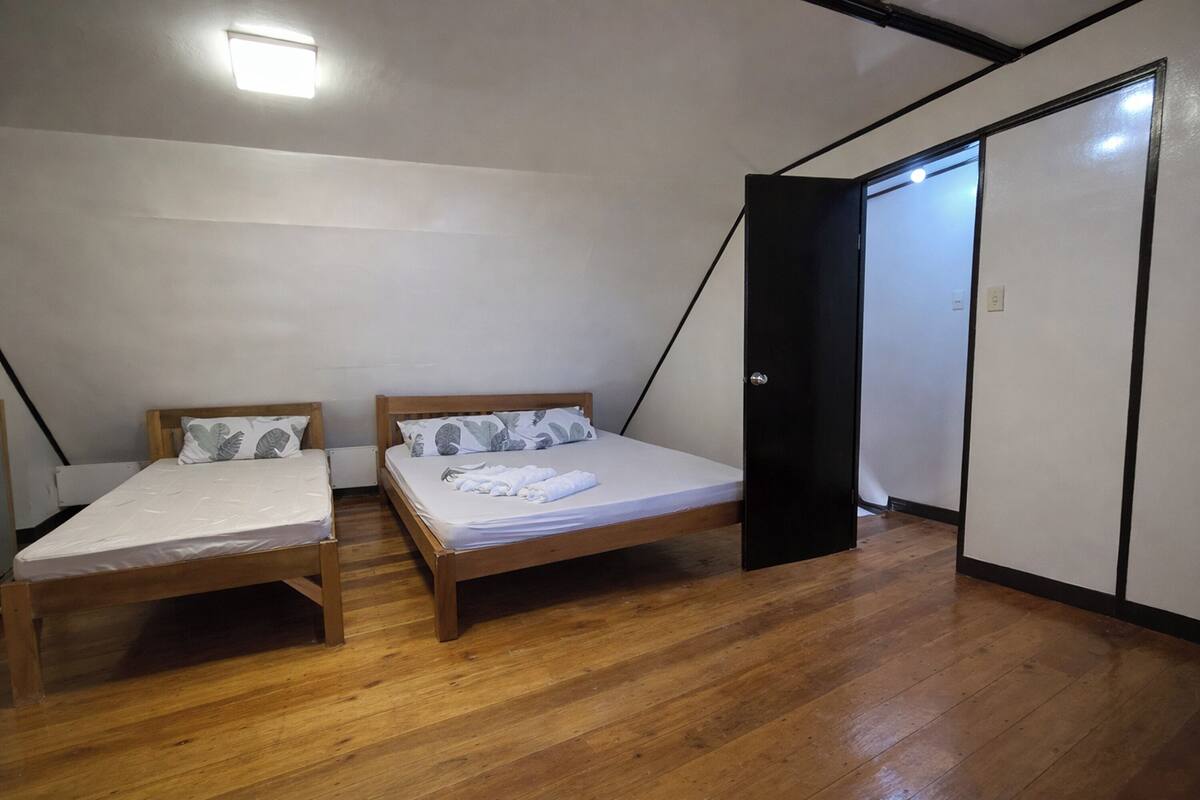 A room with two wooden beds, a black wardrobe, and a sloped ceiling.