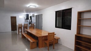 A dining area with a wooden table and chairs, a built-in bench, a window with blinds, and a wooden shelf unit. - Angelito's Beach House Siargao near Beach (General Luna)