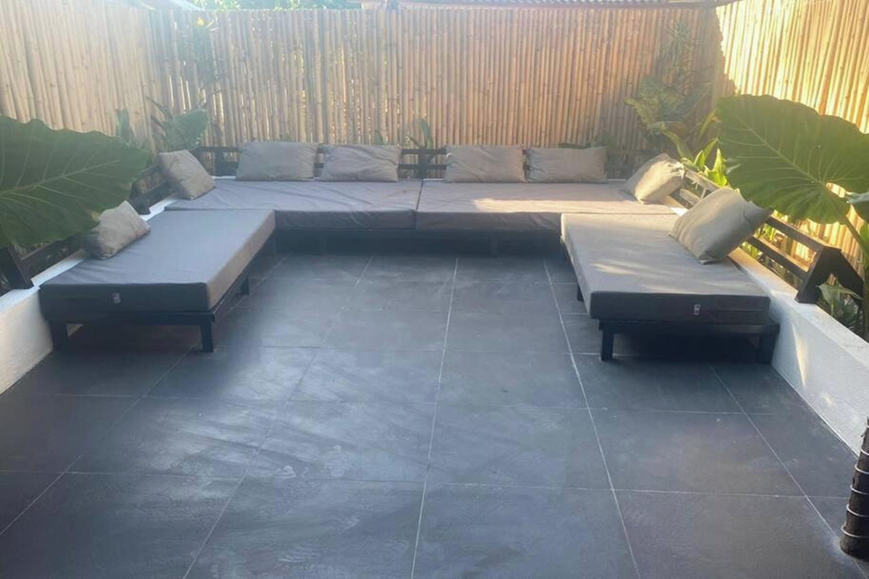 A patio with two lounge areas, a bamboo fence, and potted plants.