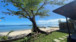 A beach view with a tree, a wooden structure, and boats on the water. - Angelito's Beach House Siargao near Beach (General Luna)