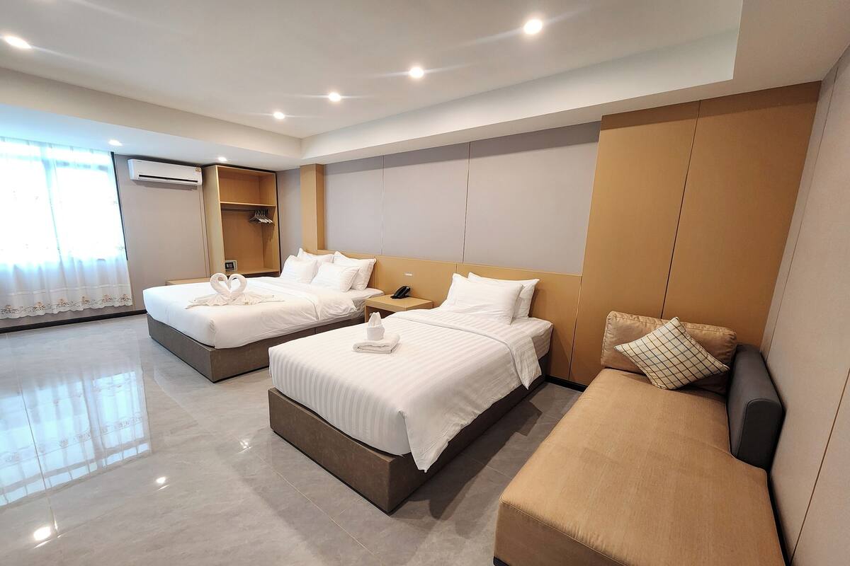 Une chambre d’hôtel avec deux lits, un canapé, une armoire et un miroir.