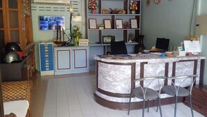 Un espace d’accueil comprenant un comptoir en marbre, deux tabourets de bar, un téléviseur, une horloge et une étagère o ù sont exposés des certificats encadrés.